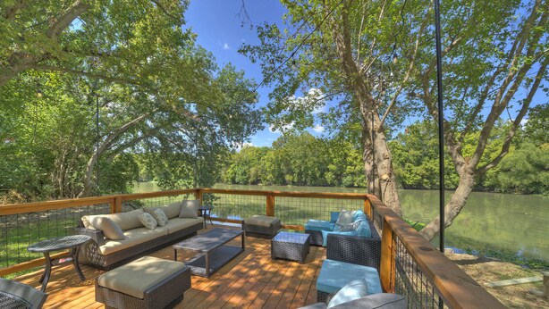 A deck with outdoor furniture, a wooden railing, and a view of a lake. - River Bend Bliss: Where Memories flow with the River (Cedar Creek)