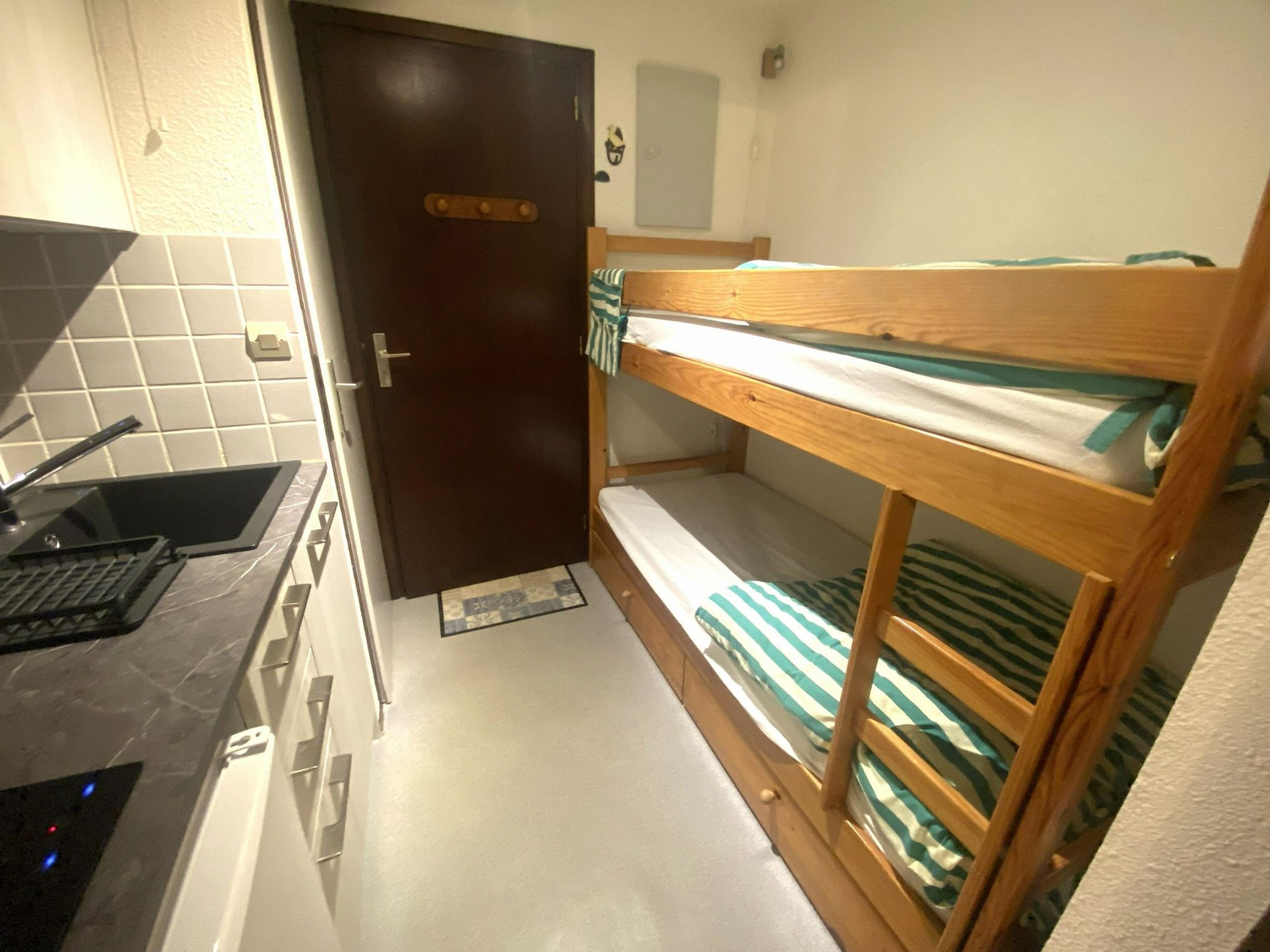 A compact room with a bunk bed, a small kitchenette with a sink, and a door.