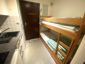 A compact room with a bunk bed, a small kitchenette with a sink, and a door.