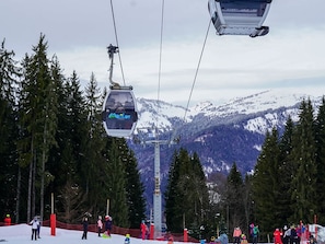 A ski lift with a chair labeled 'Maitron' in a snowy mountainous area with trees and a crowd of people.