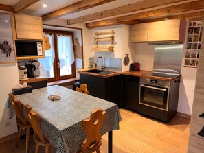 Eine kleine Küche mit Esstisch, Holzkästen, einem Einbauofen und einem Kühlschrank.