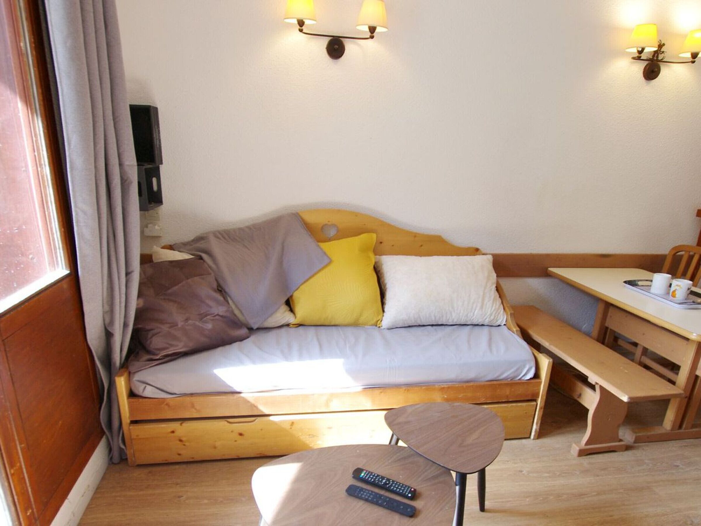 Una habitación acogedora con un sofá de madera, una mesita, un banco y una lámpara de pared.