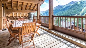 A wooden deck with a table and chairs, overlooking a mountainous landscape.