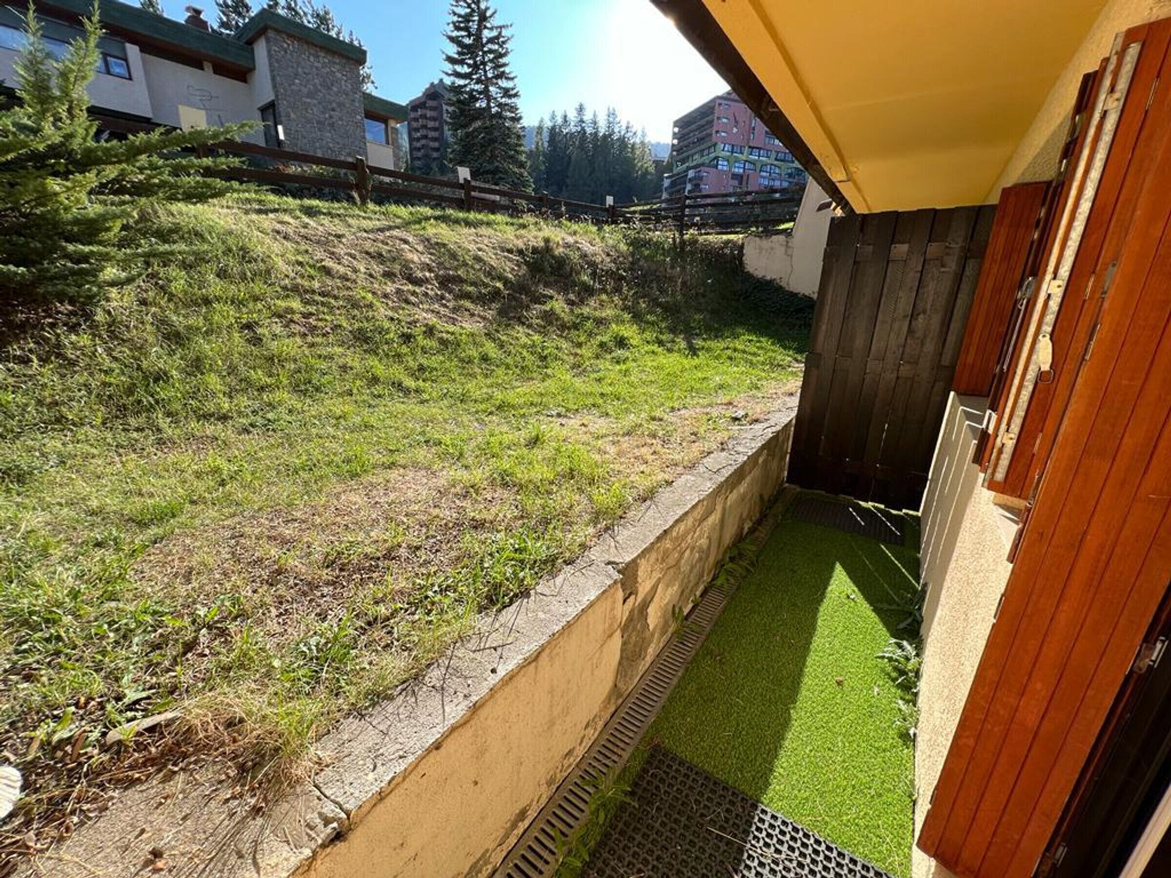 A small, enclosed outdoor area with artificial grass, a concrete retaining wall, and a wooden fence.