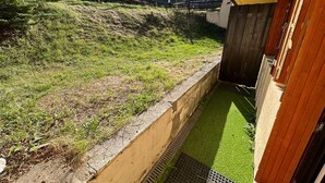 A small, enclosed outdoor area with artificial grass, a concrete retaining wall, and a wooden fence. - Spacious apartment for 8, garden and WIFI, near shops in Pra Loup (Pra-Loup)
