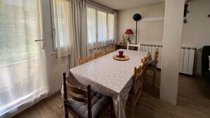 A dining area with a table set for four, wooden chairs, a red cup, and a Christmas tree on a side table. - Spacious apartment for 8, garden and WIFI, near shops in Pra Loup (Pra-Loup)