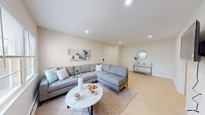 Ein modernes Wohnzimmer mit einem grauen Ecksofa, einem runden Couchtisch und einem Wand-Fernseher.
