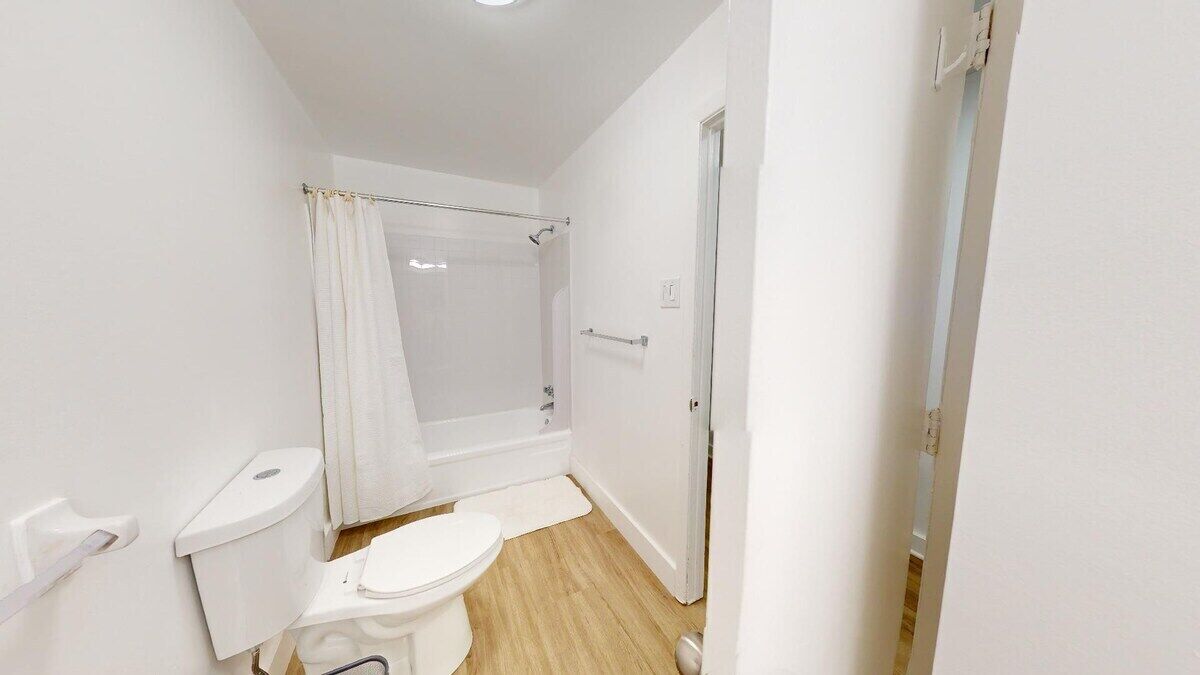 Un baño pequeño y blanco con inodoro, ducha y puerta.