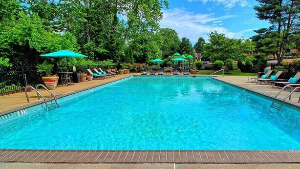 A rectangular outdoor swimming pool with a tiled deck, surrounded by lounge chairs and umbrellas.