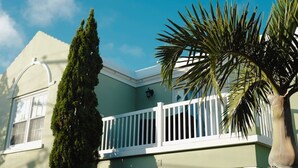 A house with a white balcony, a tall coniferous tree, and a palm tree. - This apartment is a 1 bedroom(s), 1.5 bathrooms, located in Warwick, Warwick Parish. (Warwick)