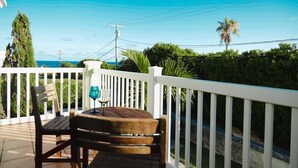 A wooden deck with a table and chairs, overlooking a road and greenery. - This apartment is a 1 bedroom(s), 1.5 bathrooms, located in Warwick, Warwick Parish. (Warwick)