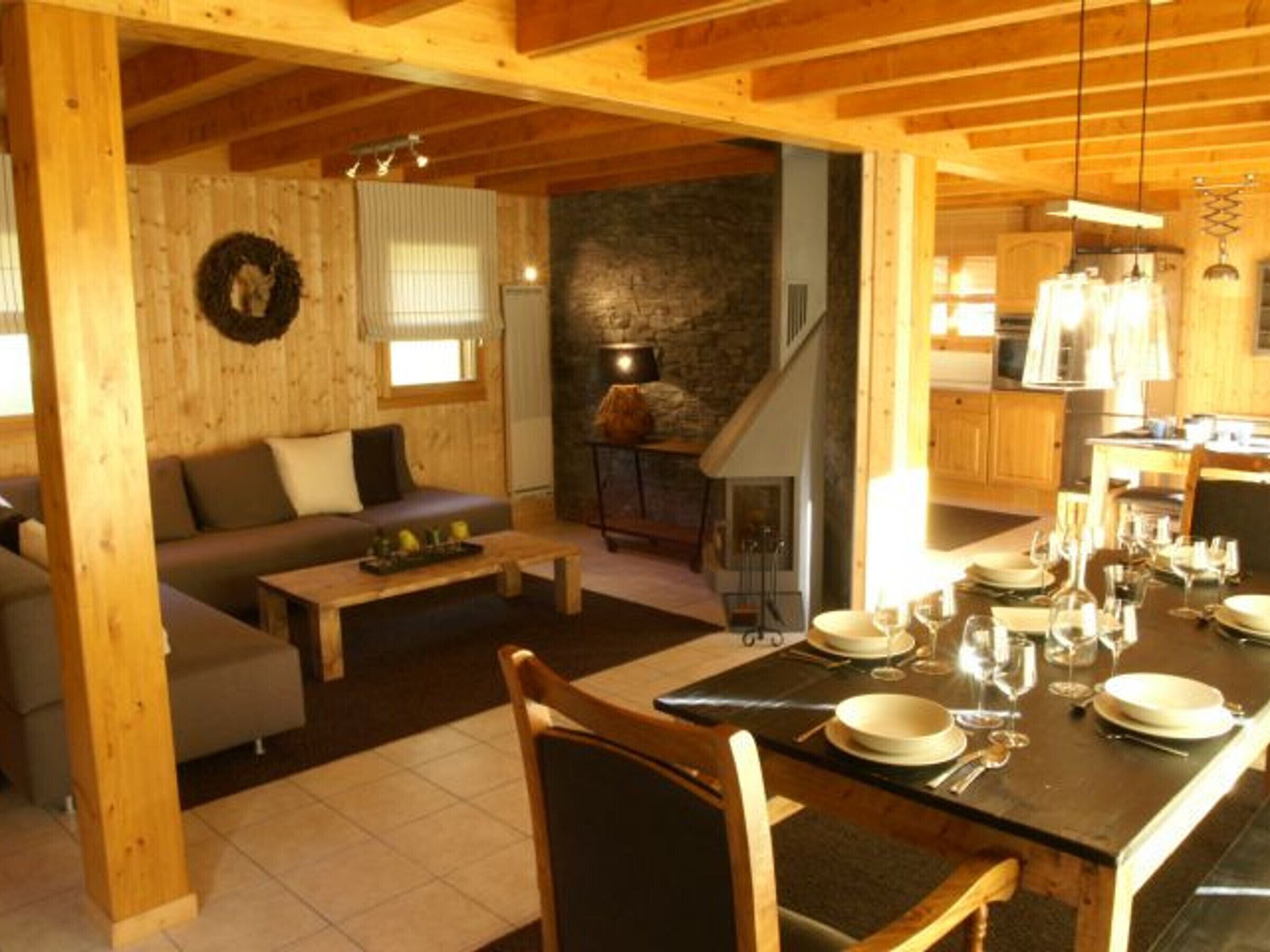 Un accogliente interno in legno con zona pranzo apparecchiata, un soggiorno con divano e camino, e una cucina visibile sullo sfondo.
