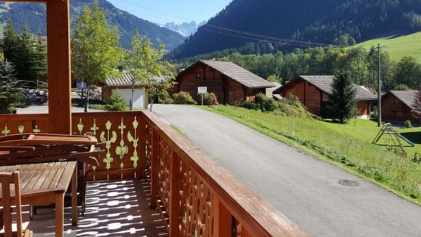 Un balcon en bois offrant une vue sur un paysage montagneux, avec plusieurs chalets en bois et un ciel dégagé.