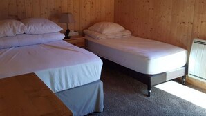 Une chambre avec deux lits, des murs en bois, une table de chevet avec une lampe et un radiateur.
