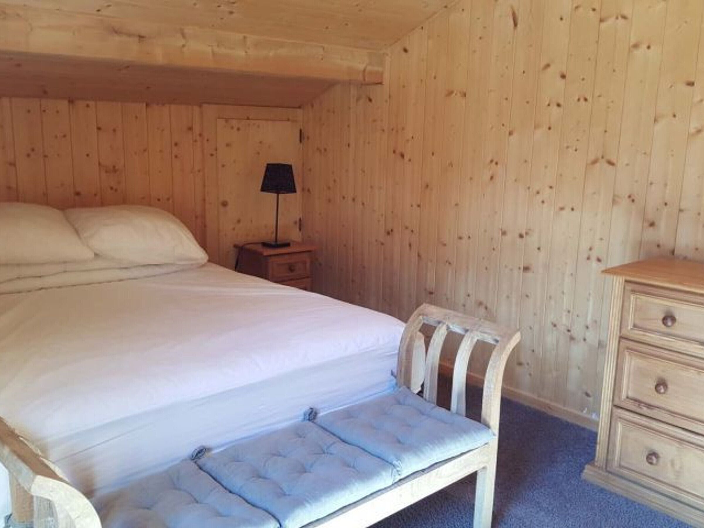 Ein Schlafzimmer mit einem Bett, einem Nachttisch mit Lampe, einer Bank und einer Kommode.