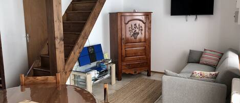 A living room with a wooden staircase, a TV mounted on the wall, a grey sofa, and a wooden cabinet with decorative carvings.