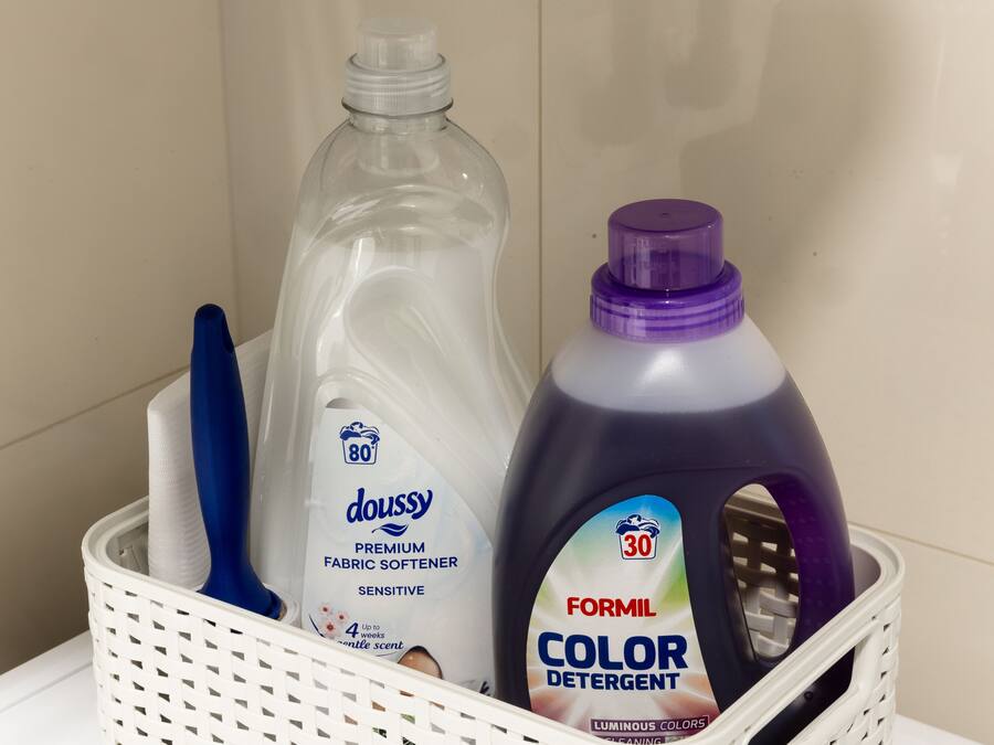 A basket containing a bottle of Doussy fabric softener, a bottle of Formil color detergent, and a blue-handled brush.