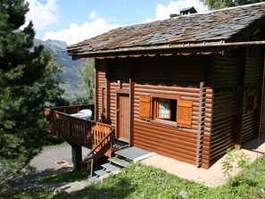 Una cabaña de madera rústica con balcón, un pequeño porche y vistas a las montañas.