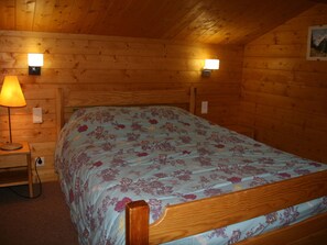 Habitación de cabaña de madera con una cama, dos lámparas fijadas a la pared y una mesita de noche con lámpara.