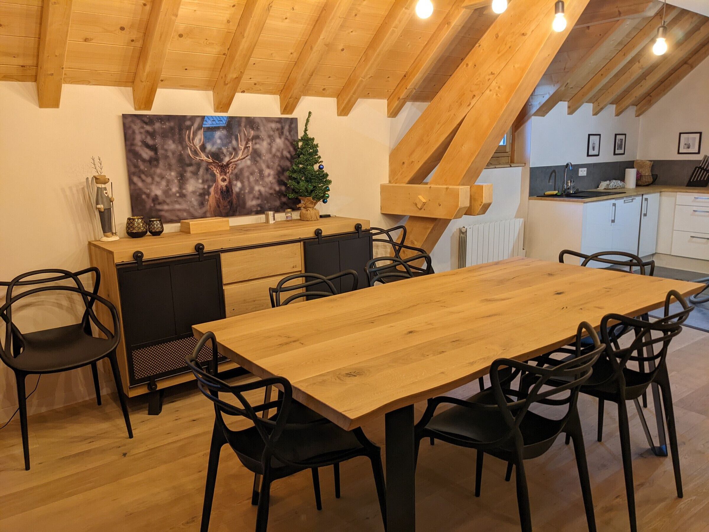 Ein Essbereich mit Holztisch und -stühlen, einem an der Wand montierten Fernseher und einer Küche im Hintergrund.