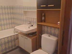Um banheiro com pia branca, banheira, vaso sanitário e armários de madeira.