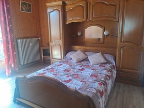 Quarto com cabeceira de madeira, cama com colcha estampada, duas almofadas, mesa de cabeceira e espelho sobre a cama.
