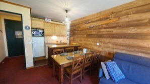 Een kleine keuken met houten kastjes, een eettafel met stoelen en een blauwe bank.