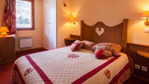 Een bed met een quilt, een nachtkastje, een wandlamp en een raam met gordijnen.