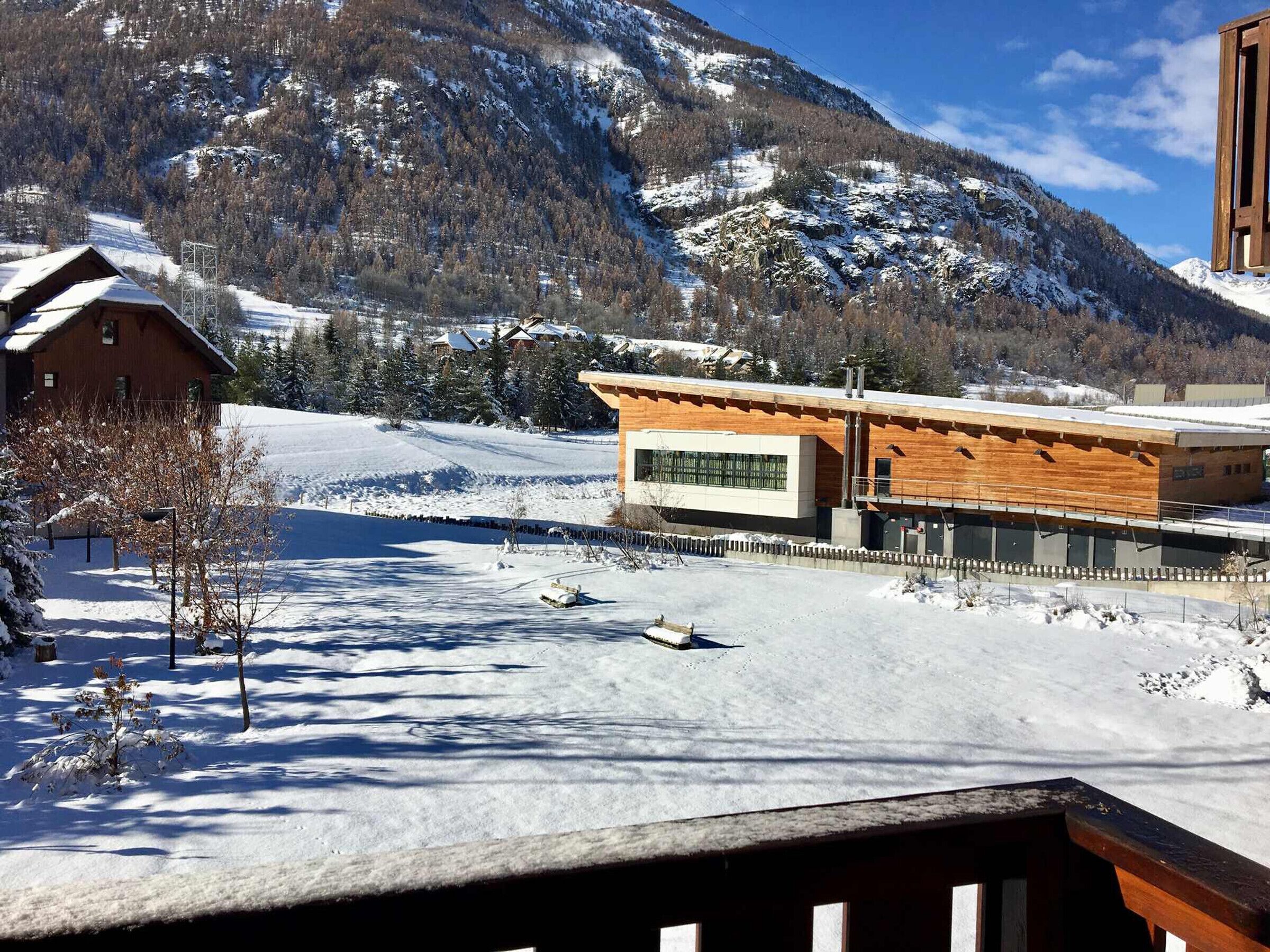 A modern building with a wooden facade, a snow-covered landscape, and mountains in the background.