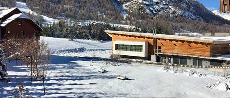 A modern building with a wooden facade, a snow-covered landscape, and mountains in the background.