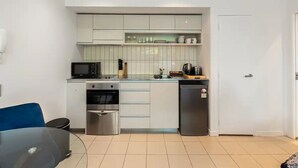A compact kitchen with white cabinets, a microwave, oven, and a refrigerator. - Charming 1BR in Wynyard Quarter I Zodiak Stays (Auckland)
