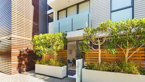 A modern building with a glass entrance, wooden slatted walls, and a small outdoor seating area with benches and plants. - Charming 1BR in Wynyard Quarter I Zodiak Stays (Auckland)