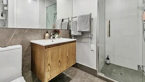 Une salle de bain moderne avec un meuble-lavabo en bois, une cabine de douche en verre et un grand miroir.