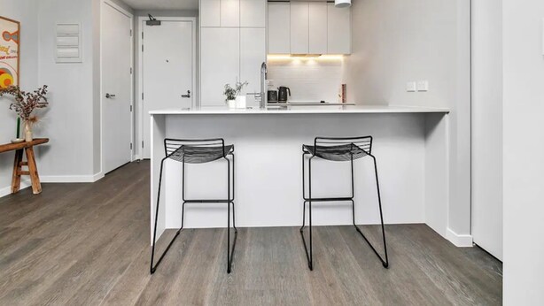 Une cuisine moderne avec des meubles blancs, un îlot central doté de deux tabourets de bar et un luminaire suspendu au-dessus.