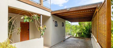 A modern house with a covered patio, a wooden door, and a view of greenery.