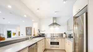 A modern kitchen with stainless steel appliances, a central island, and recessed lighting. - Stylish And Serene Living In Kohimarama (Auckland)