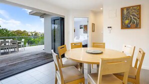 A modern dining area with a round table and chairs, a glass door leading to a balcony, and a painting on the wall. - Stylish And Serene Living In Kohimarama (Auckland)