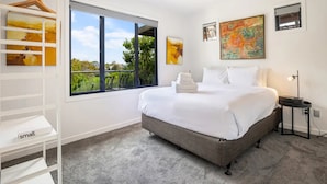 A bedroom with a large window, a bed, a bedside table, and a hanging rack with towels. - Stylish And Serene Living In Kohimarama (Auckland)