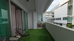 A balcony with artificial grass, two black chairs, a small table, and a window with curtains. - Viaduct apartment with a balcony by Zodiak Stays (Auckland)
