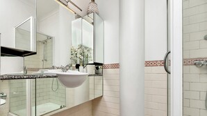 A bathroom with a glass shower enclosure, a sink with a mirror, and a decorative vase with flowers. - Viaduct apartment with a balcony by Zodiak Stays (Auckland)