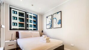 A modern bedroom with a large bed, a nightstand, a lamp, and two abstract paintings on the wall. - Central & Modern 2-Bedroom Apartment (Auckland)