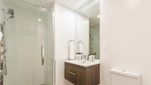 A modern bathroom with a glass shower enclosure, a wooden vanity with a mirror, and a toilet. - Central & Modern 2-Bedroom Apartment (Auckland)