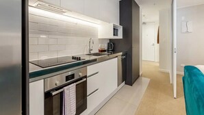 A modern kitchen with white cabinets, a stainless steel range, a microwave, and a black accent wall. - Central & Modern 2-Bedroom Apartment (Auckland)