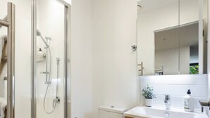 Un baño moderno con ducha envuelta en vidrio, inodoro, lavamanos con espejo y muebles de madera.