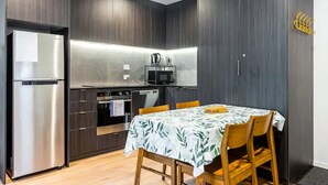 A compact kitchen with dark wood cabinets, a stainless steel refrigerator, and a microwave. - Auckland City Charm - 2BR Haven by Zodiak Stays (Auckland)
