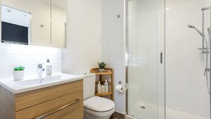 A modern bathroom with a white sink, wooden vanity, toilet, and a glass-enclosed shower area. - Auckland City Charm - 2BR Haven by Zodiak Stays (Auckland)