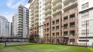 Ein Tennisplatz, umgeben von mehrstöckigen Wohnhäusern mit Balkonen.
