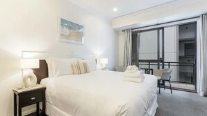 Ein Hotelzimmer mit einem großen Bett, einem Nachttisch, einem Sessel und Blick nach draußen durch eine Schiebetür.