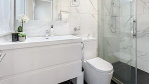 A modern bathroom with a marble vanity, a toilet, a glass shower enclosure, and a large mirror. - Parnell Home With Stunning Views (Auckland)