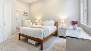 A bedroom with a bed, bedside tables, a nightstand, a dresser, a window, and a door. - Parnell Home With Stunning Views (Auckland)